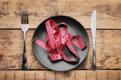 Photo of Plate with measuring tape served on wooden table, flat lay. Weight loss concept