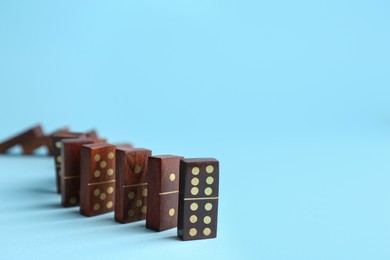 Photo of Row of wooden domino tiles on light blue background. Space for text