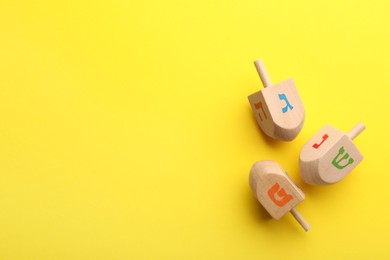 Photo of Wooden dreidels on yellow background, above view with space for text. Traditional Hanukkah game