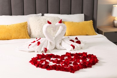 Photo of Honeymoon. Swans made with towels and heart of beautiful rose petals on bed in room