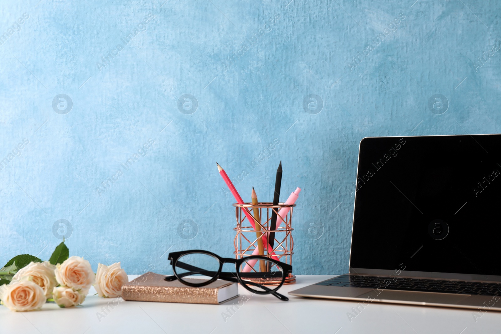 Photo of Comfortable workplace with modern laptop, stationery and flowers near light blue wall. Space for design