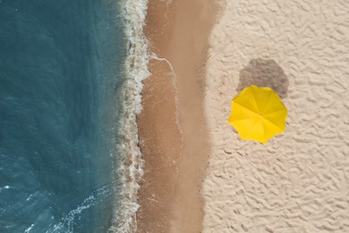 Image of Yellow beach umbrella on sandy coast near sea, top view