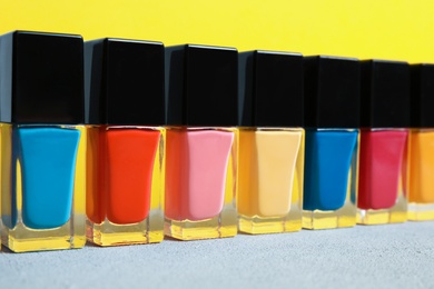 Photo of Bright nail polishes on table against color background, closeup