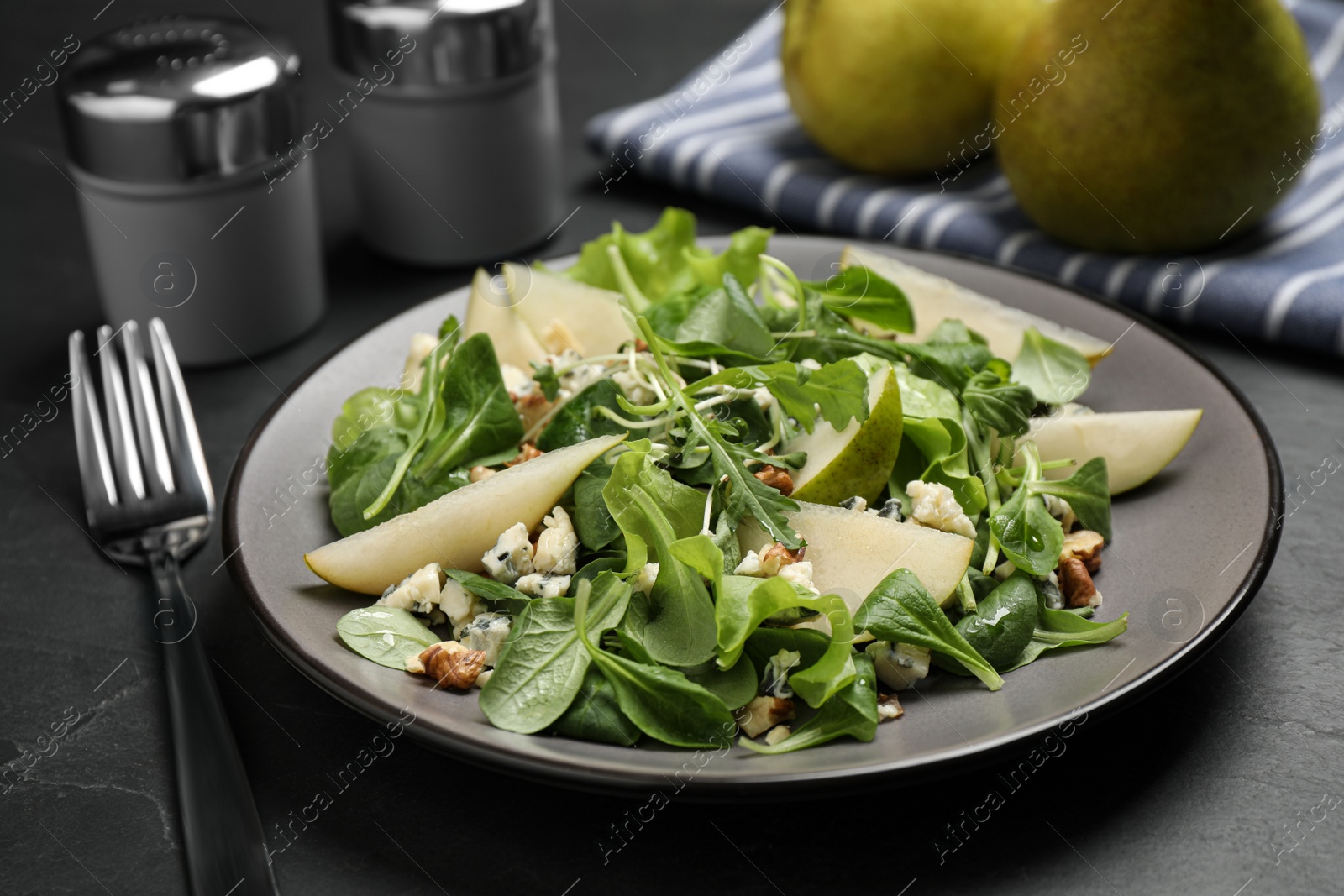 Photo of Tasty salad with pear slices and fork on black table, closeup