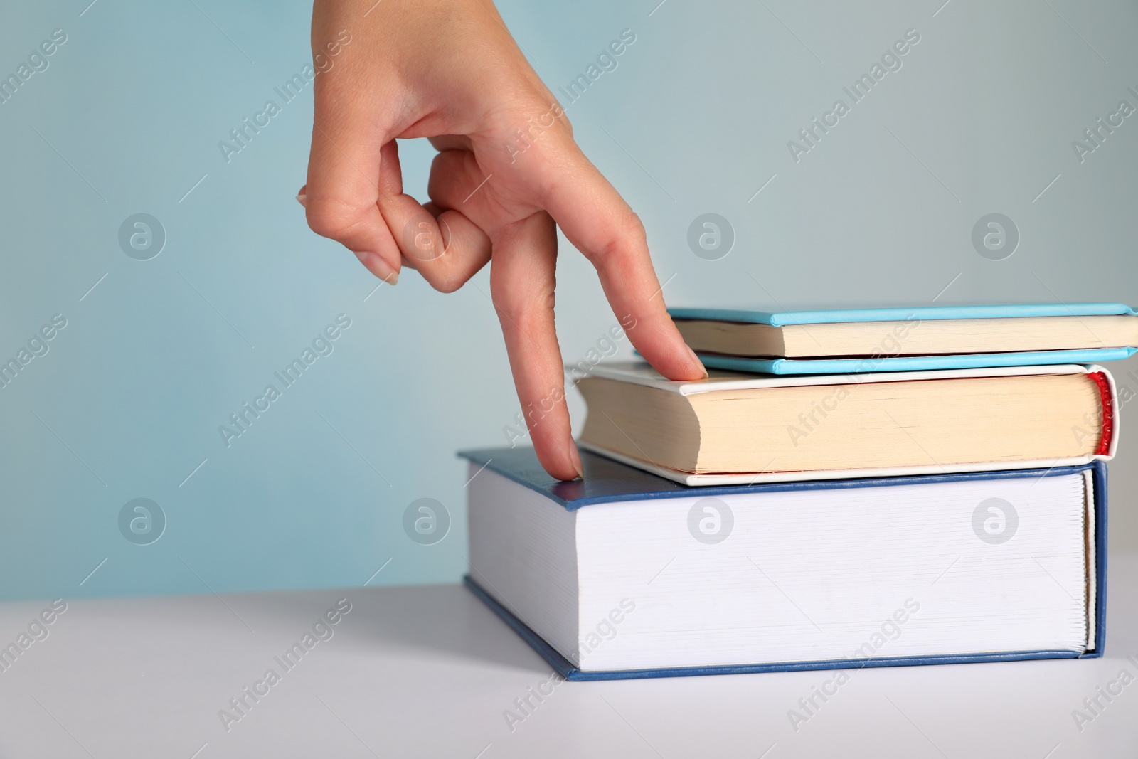 Woman imitating stepping up on books with her fingers against light blue background, closeup Photo of Woman imitating stepping up on books with her fingers against light blue background, closeup