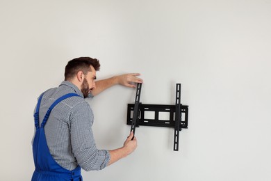 Photo of Professional technician installing TV bracket on wall indoors
