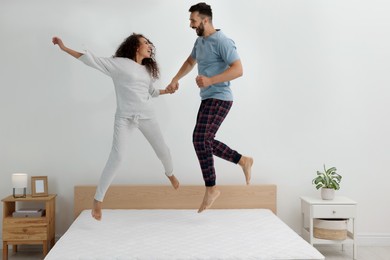 Photo of Happy couple jumping on bed with comfortable mattress at home