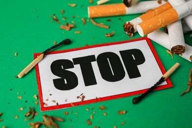 Photo of Stop smoking concept. Card with word Stop, cigarette stubs, tobacco and burnt matches on green background, closeup