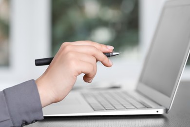 Photo of Woman with pen working on laptop, closeup. Electronic document management