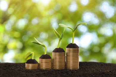Image of Stacked coins and green seedlings on ground outdoors, bokeh effect. Investment concept