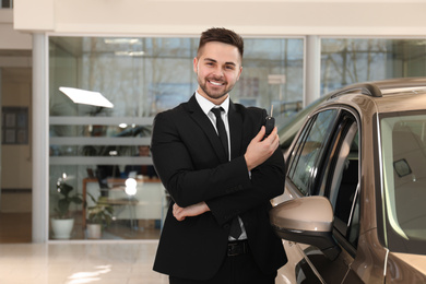 Photo of Young salesman with key near car in dealership
