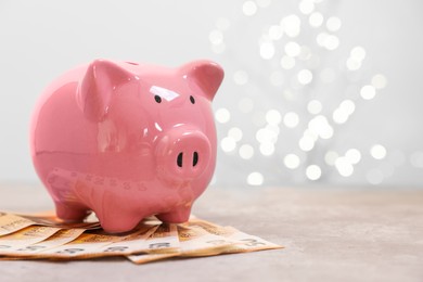 Photo of Piggy bank with euro banknotes on grey table against blurred lights, space for text