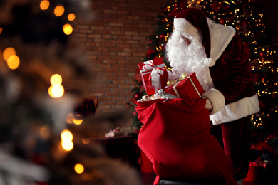 Photo of Santa Claus packing gifts into bag near Christmas tree