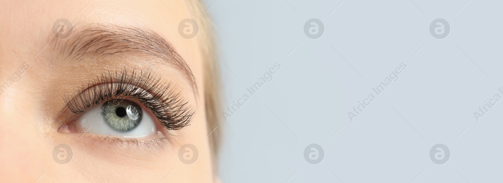 Image of Closeup view of young woman with beautiful long eyelashes on light background, space for text. Banner design