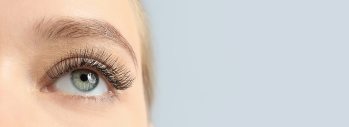 Image of Closeup view of young woman with beautiful long eyelashes on light background, space for text. Banner design