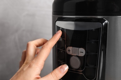 Photo of Woman turning on modern electric multi cooker on grey background, closeup