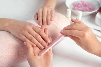 Photo of Manicurist filing client's nails at table, closeup. Spa treatment