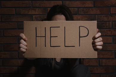 Photo of Young woman with sign HELP near brick wall. Domestic violence concept