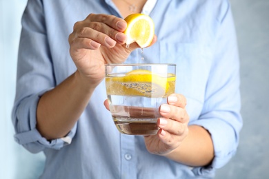 Photo of Woman squeezing lemon juice into glass of soda water, closeup