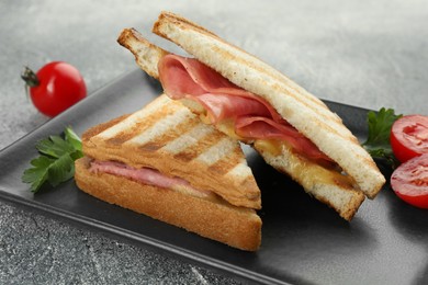 Photo of Tasty sandwiches with ham, parsley, tomatoes and melted cheese on grey textured table, closeup