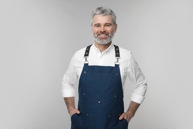 Photo of Happy man wearing kitchen apron on grey background. Mockup for design