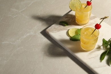 Photo of Glasses of tasty pineapple cocktail decorated with cherry and lime on light grey marble table. Space for text