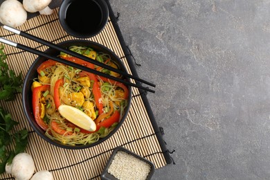 Photo of Stir-fry. Delicious cooked noodles with chicken and vegetables in bowl served on gray textured table, flat lay. Space for text