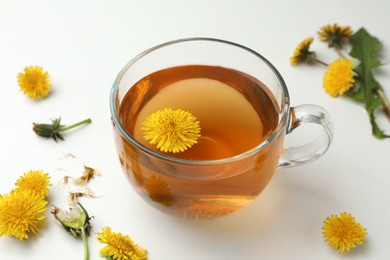 Photo of Delicious fresh tea and beautiful dandelion flowers on white table