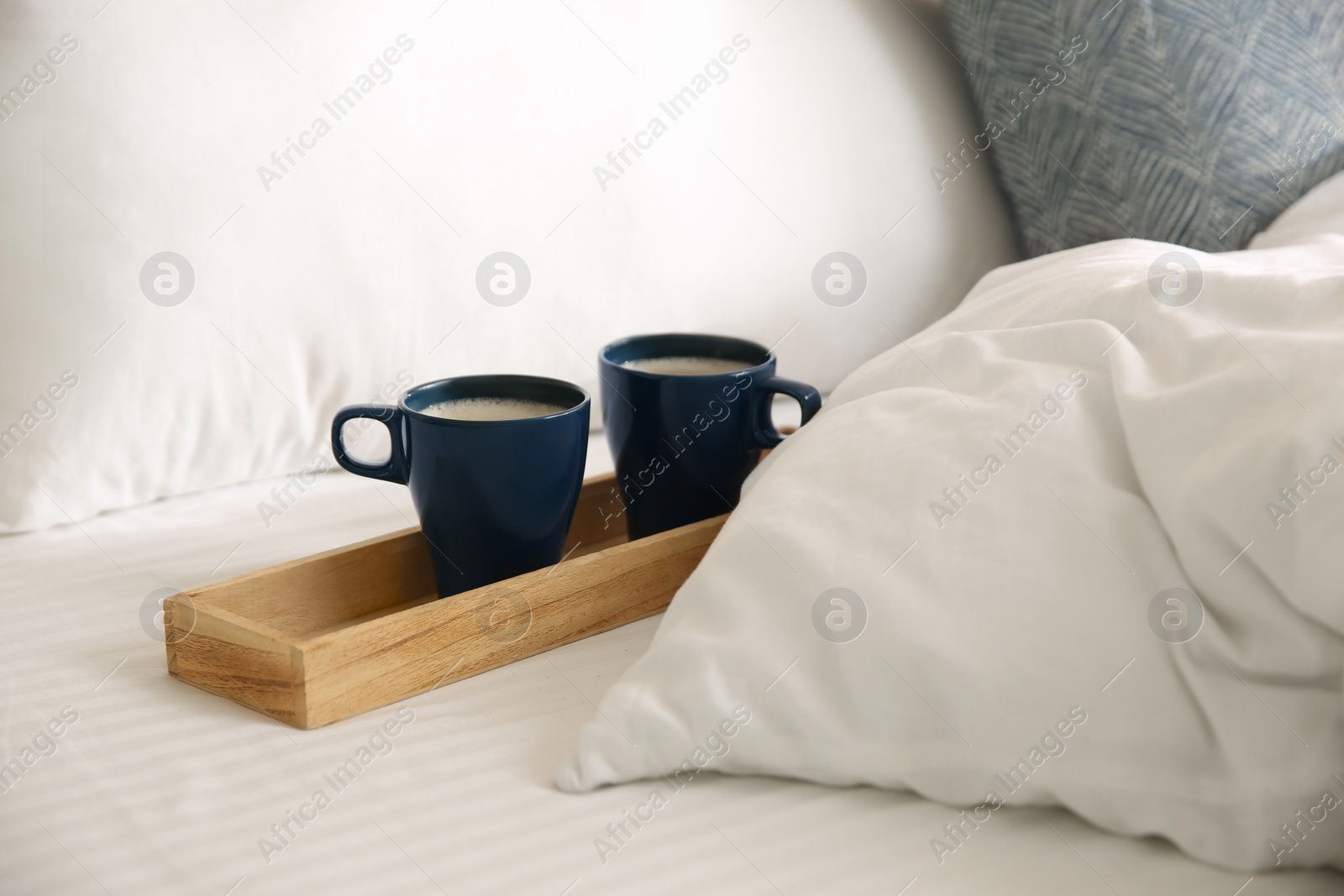 Photo of Wooden tray with cups of coffee near soft blanket on bed