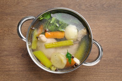 Photo of Pot with tasty bouillon on wooden table, top view