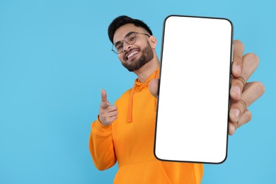 Image of Happy man holding smartphone with empty screen on light blue background, space for text