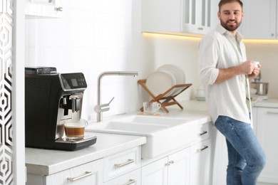Photo of Young man enjoying fresh aromatic coffee in kitchen, focus on modern machine