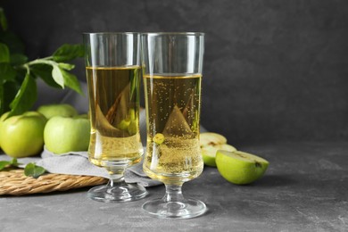 Photo of Glasses of delicious cider and green apples on gray table