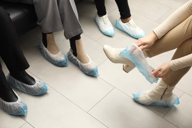 Women wearing blue shoe covers onto different footwear indoors, closeup