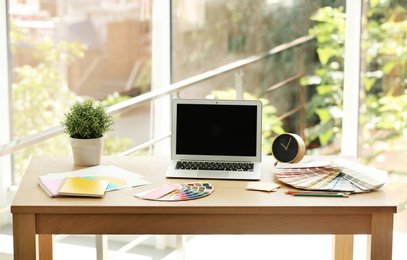 Photo of Designer's workplace with laptop and paint color palette samples on table