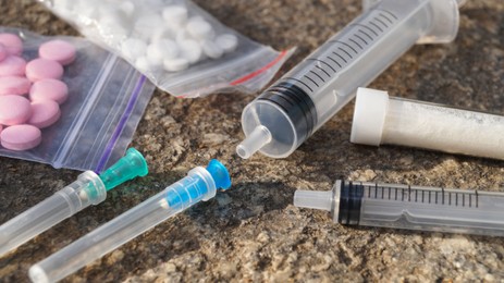 Photo of Plastic bags with pills, syringes and powder on stone surface, closeup. Hard drugs