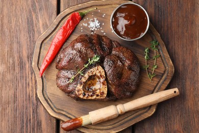 Photo of Delicious roasted beef meat served with sauce and spices on wooden table, top view