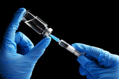 Photo of Doctor filling syringe with medication on black background, closeup. Vaccination and immunization