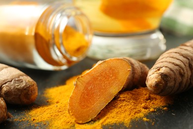 Photo of Turmeric roots, powder and cup of tasty tea on black table, closeup