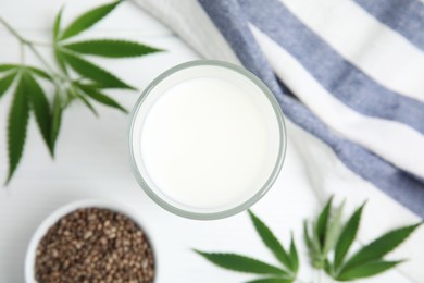 Photo of Glass of fresh hemp milk, seeds and leaves on white table, flat lay