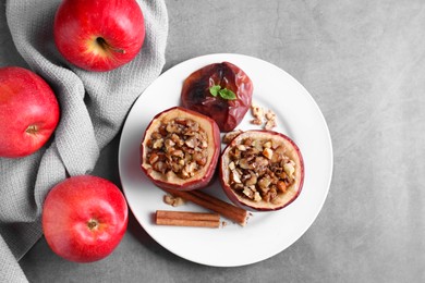 Photo of Tasty baked apples with nuts, honey, cinnamon sticks and mint on gray table, flat lay