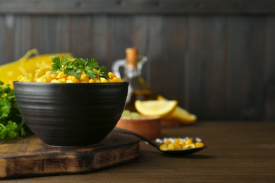Photo of Bowl with tasty boiled corn on wooden table. Space for text