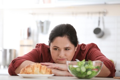Photo of Woman choosing between vegetable salad and dessert in kitchen. Healthy diet