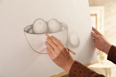 Photo of Woman drawing bowl of fruits with graphite pencil on canvas indoors, closeup