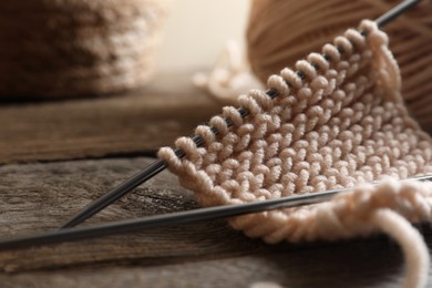 Soft beige knitting and metal needles on wooden table, closeup
