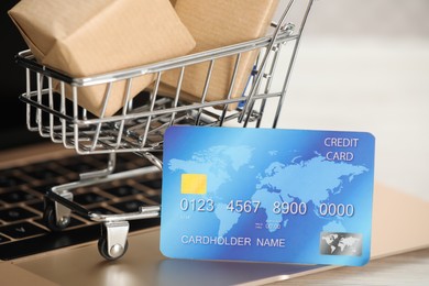 Photo of Online payment concept. Small shopping cart with bank card, boxes on laptop, closeup