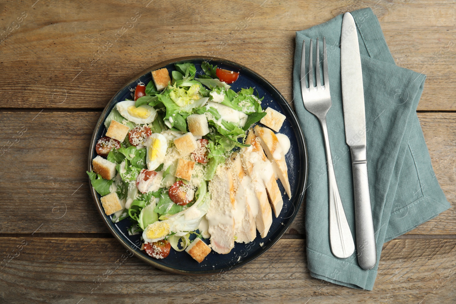 Delicious Caesar salad in bowl on wooden table, flat lay Photo of Delicious Caesar salad in bowl on wooden table, flat lay