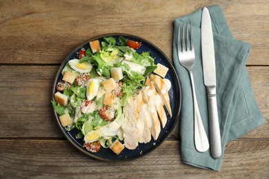 Photo of Delicious Caesar salad in bowl on wooden table, flat lay