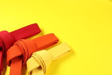 Photo of Colorful karate belts on yellow background, flat lay. Space for text
