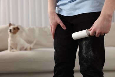 Photo of Pet shedding. Man with lint roller removing dog's hair from pants at home, closeup